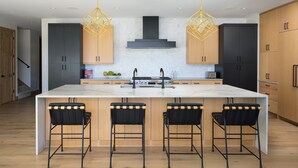 Una cocina moderna con una isla central, taburetes de bar, luces colgantes y armarios de madera.