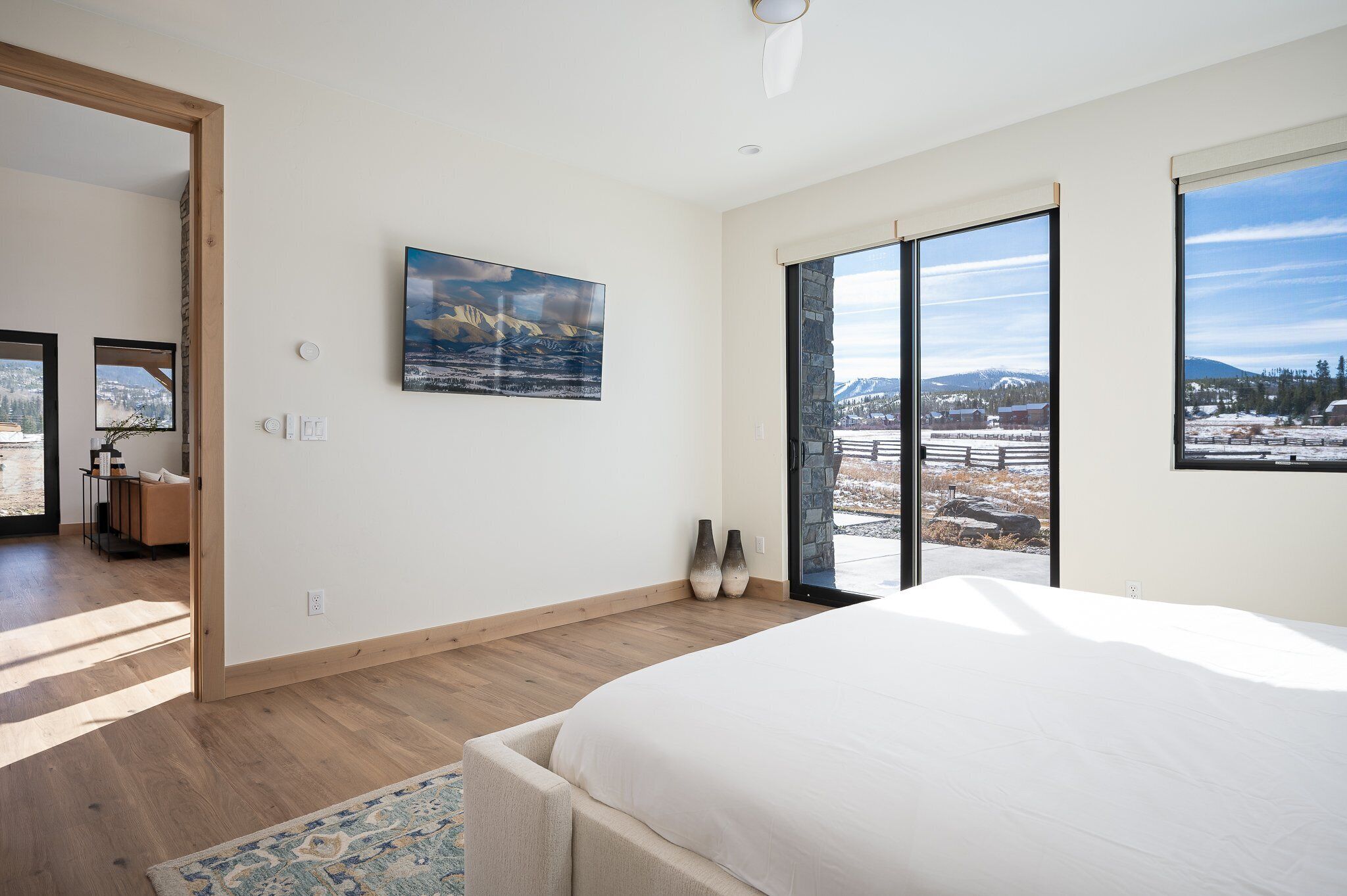A bedroom with a large bed, a view of a snowy landscape through a sliding door, and a painting on the wall.