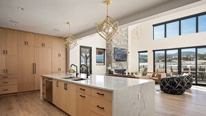 Una cocina amplia con armarios de madera, una isla de mármol y ventanas grandes con vistas a un paisaje nevado.