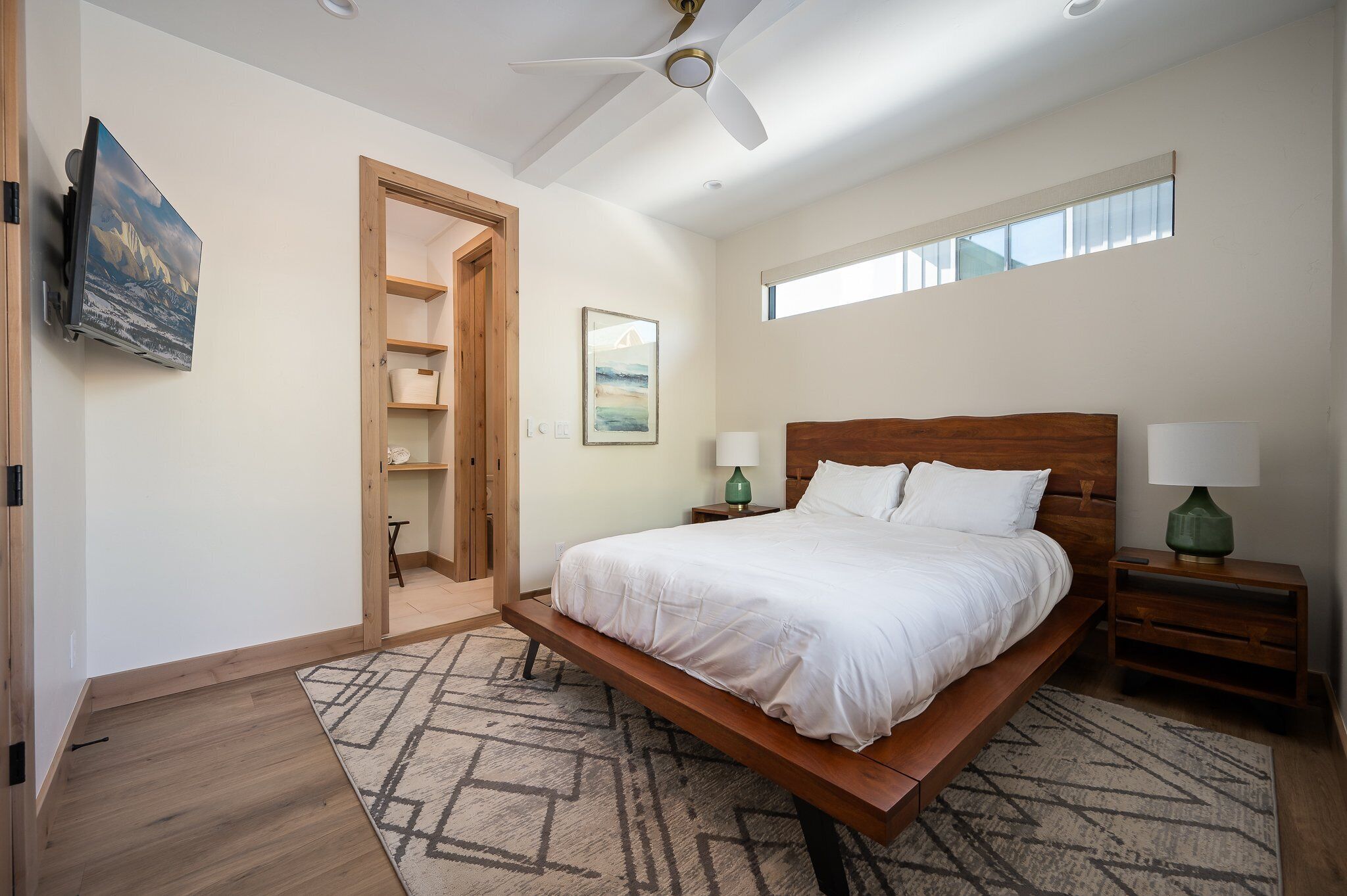 Una camera da letto con un letto, comodini, una ventola a soffitto, una finestra e un quadro appeso al muro.