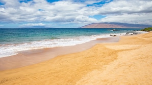 A beach with clear blue water, a sandy shore, and a mountain in the background. - Kamaole Sands Condos Close to Beach with Parking (Kihei)
