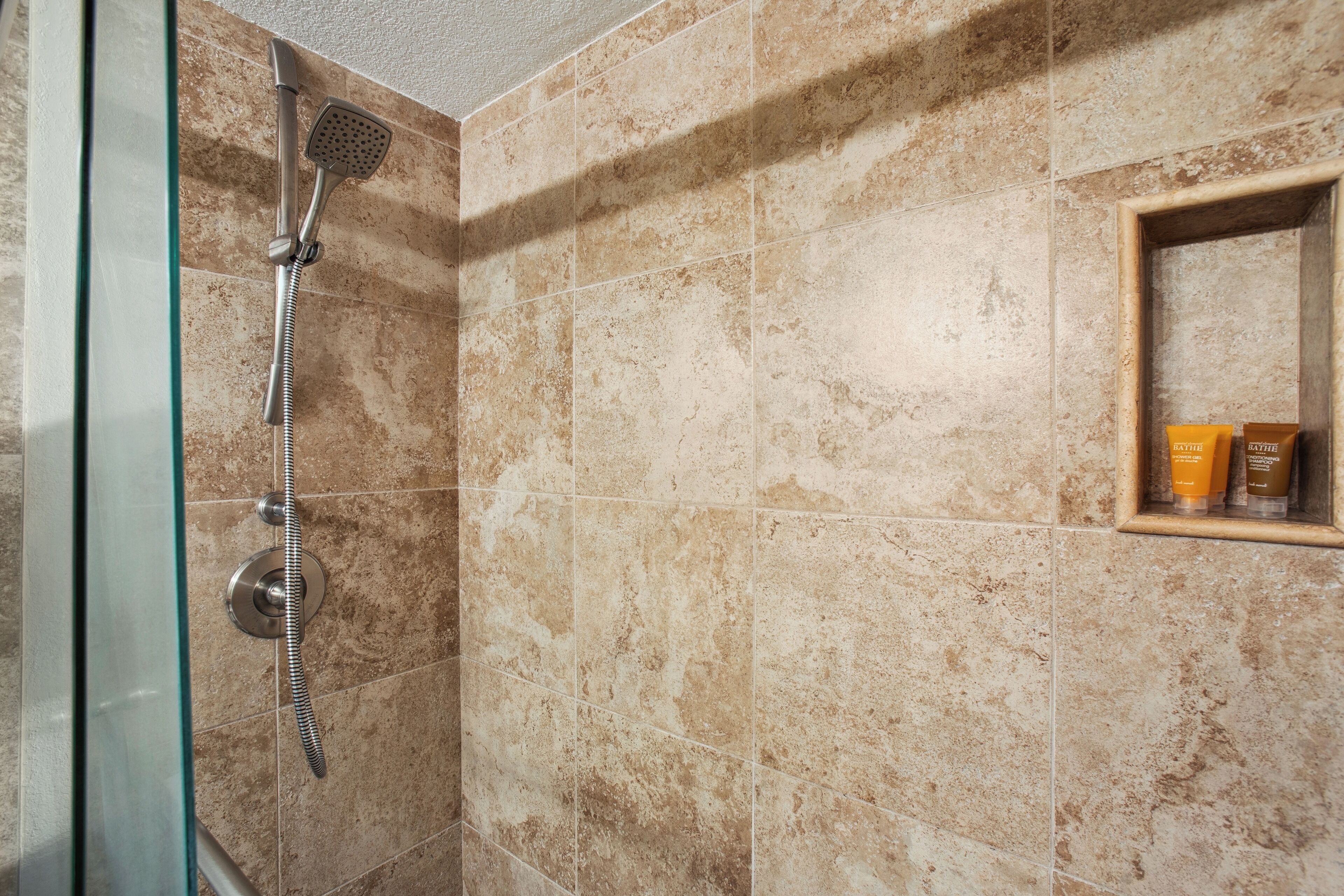 A shower with a handheld showerhead and a glass door.