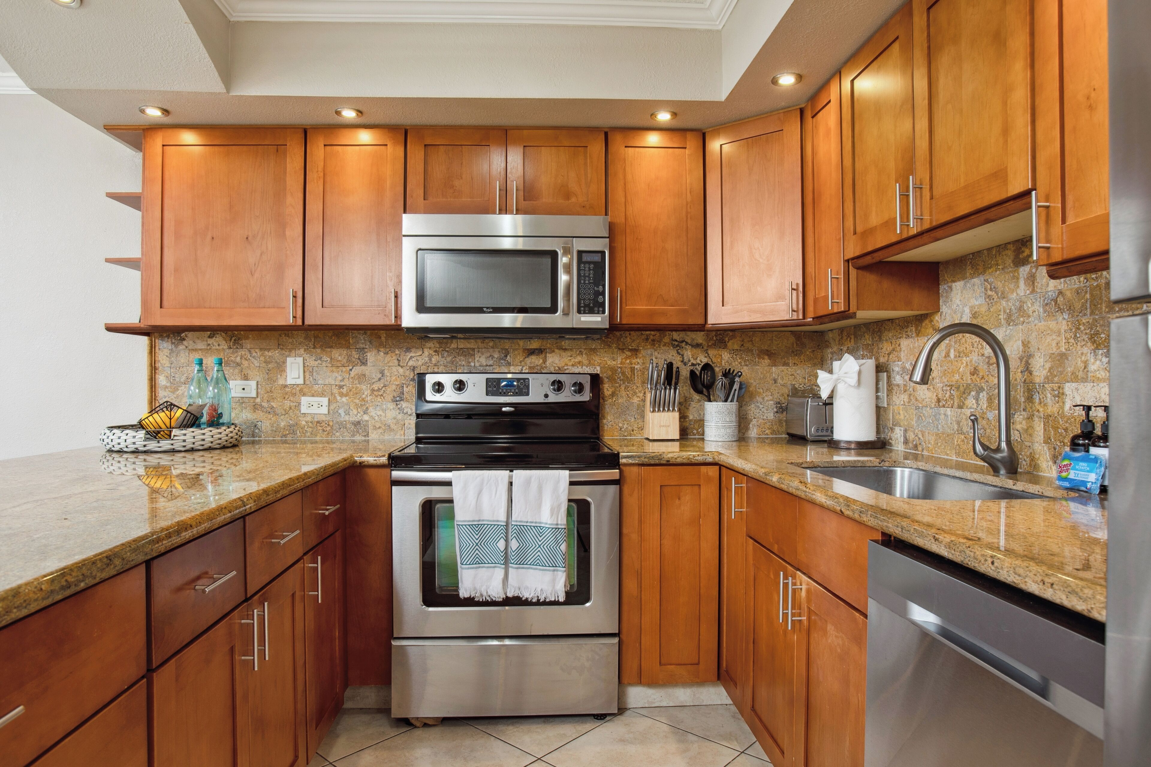A modern kitchen with wooden cabinets, stainless steel appliances, granite countertops, and a tiled backsplash.