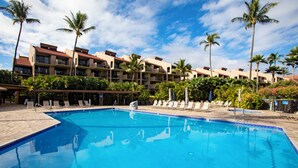 A swimming pool with lounge chairs, palm trees, and a multi-story building in the background. - Kamaole Sands Condos Close to Beach with Parking (Kihei)
