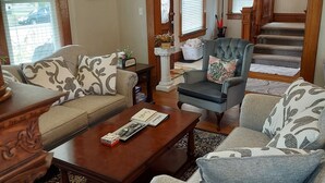 A living room with a sofa, armchairs, a coffee table, and a staircase leading to an upper floor. - Charming historical 4 bd & 3 full ba home in Terre Haute with WiFi, AC & parking (Terre Haute)