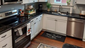 A modern kitchen with white cabinets, stainless steel appliances, a black countertop, and a wooden floor. - Charming historical 4 bd & 3 full ba home in Terre Haute with WiFi, AC & parking (Terre Haute)