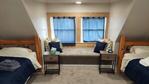 A bedroom with two single beds, a small window with curtains, a nightstand with a lamp, and a carpeted floor. - Charming historical 4 bd & 3 full ba home in Terre Haute with WiFi, AC & parking (Terre Haute)