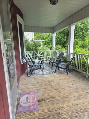 A covered porch with wooden flooring, a white railing, and two chairs.
