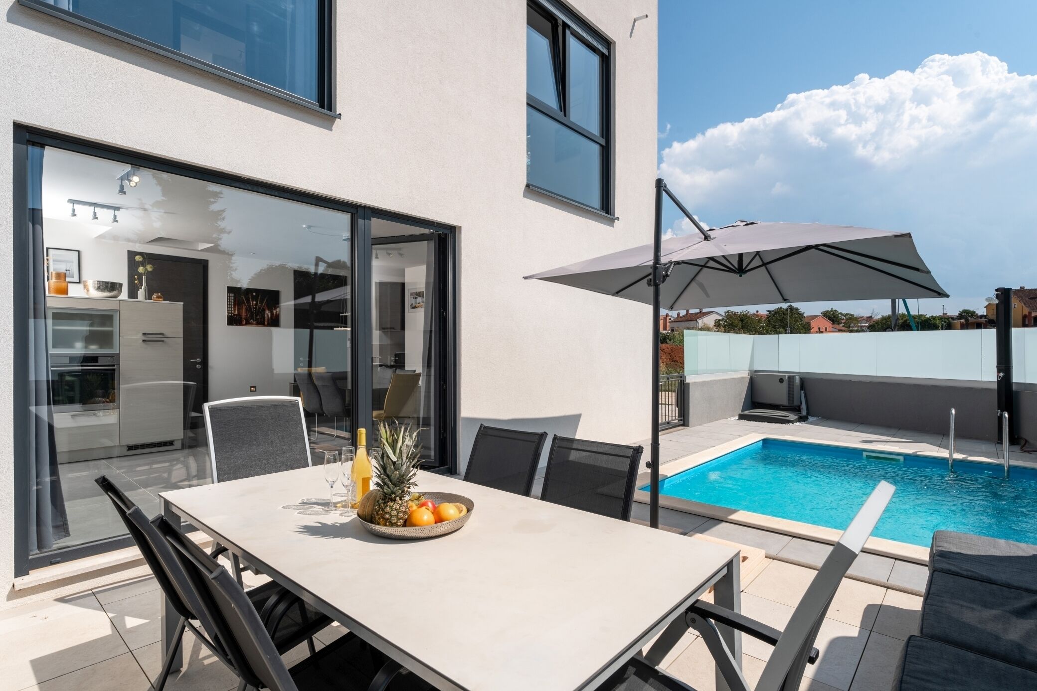 A modern outdoor dining area with a pool, a table with chairs, and a large umbrella.