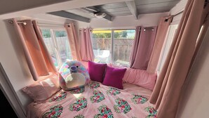 Une chambre confortable avec un lit, un grand jouet en peluche et une fenêtre avec des rideaux.