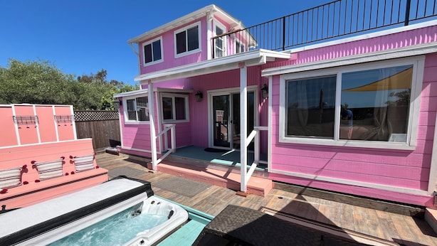 Une maison rose à deux étages, dotée d’un jacuzzi et d’un patio couvert.