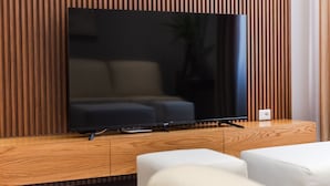 A flat-screen TV on a wooden TV stand with a modern design, a sofa, and a potted plant.