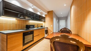 A modern kitchen with wooden cabinetry, a built-in microwave, and a dishwasher. There is a dining table with chairs in the background.
