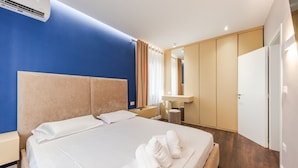 A hotel room with a large bed, a bedside table, a mirror, a wardrobe, and an air conditioning unit.
