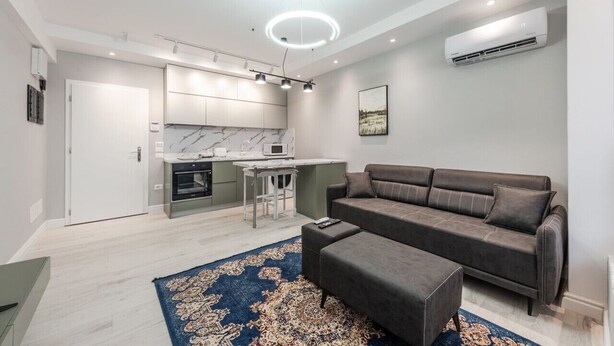 Un salon moderne avec un canapé gris, un pouf assorti et un tapis à motifs.