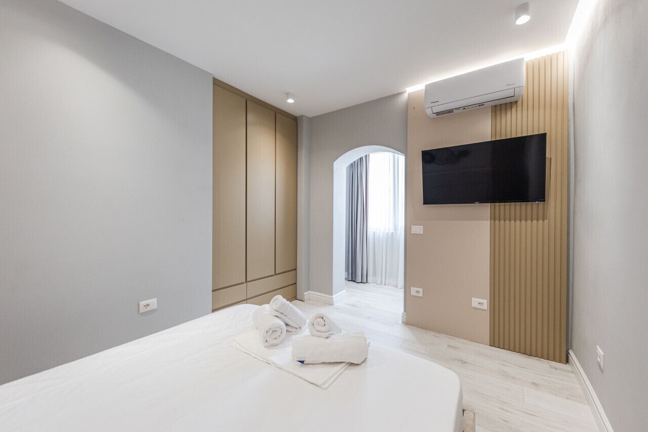 A modern hotel room with a large bed, a flat-screen TV mounted on the wall, and an air conditioning unit.