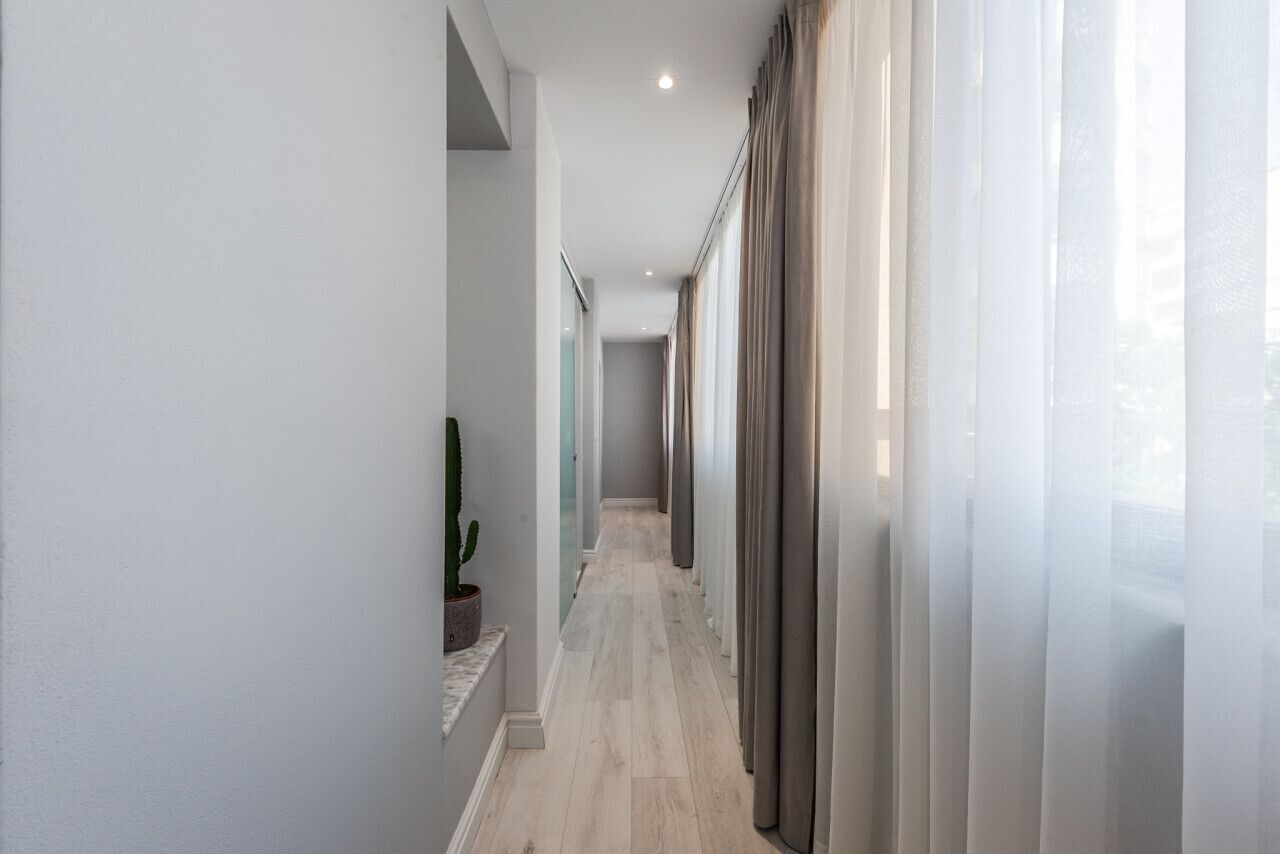 A modern hallway with a light-colored floor, a potted plant, and sheer curtains on the right.