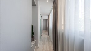 Un couloir moderne avec un plancher de couleur claire, une plante en pot et des rideaux légers sur le côté droit.