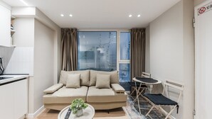 Ein modernes Wohnzimmer mit einer Couch, einem kleinen Tisch mit Pflanze, einem Essbereich mit Tisch und Stühlen sowie einer Küchenzeile mit Herd.