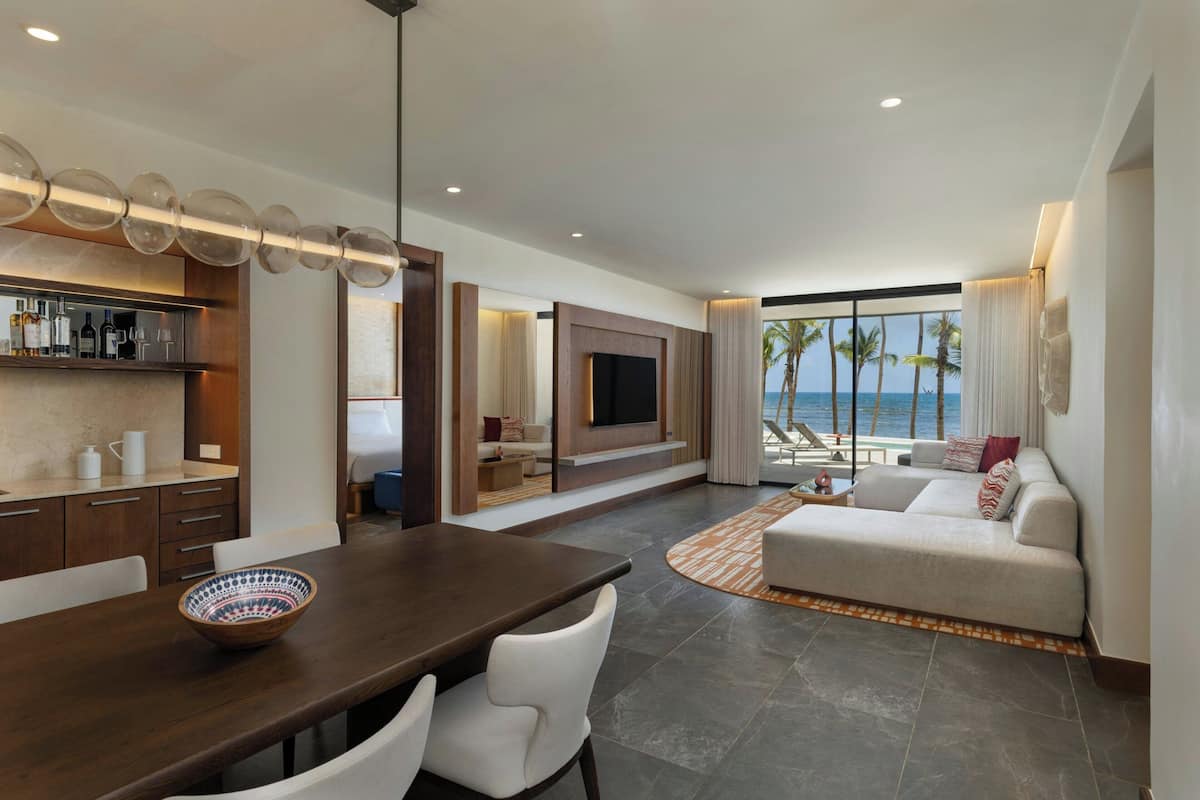 A modern living room with a dining area, a flat-screen TV, and a view of the ocean.