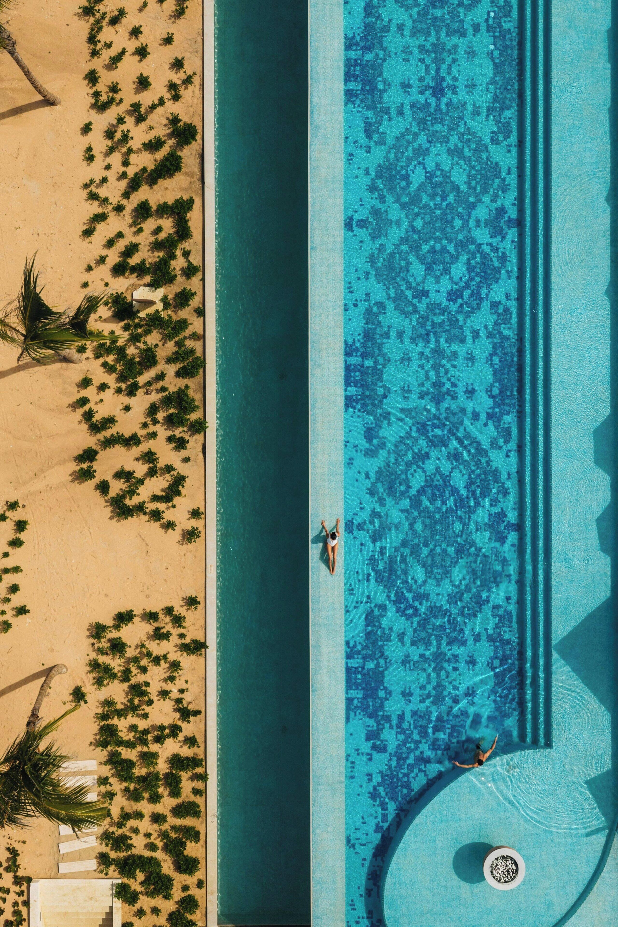 Vista aérea de una playa con piscina, palmeras y una persona nadando.
