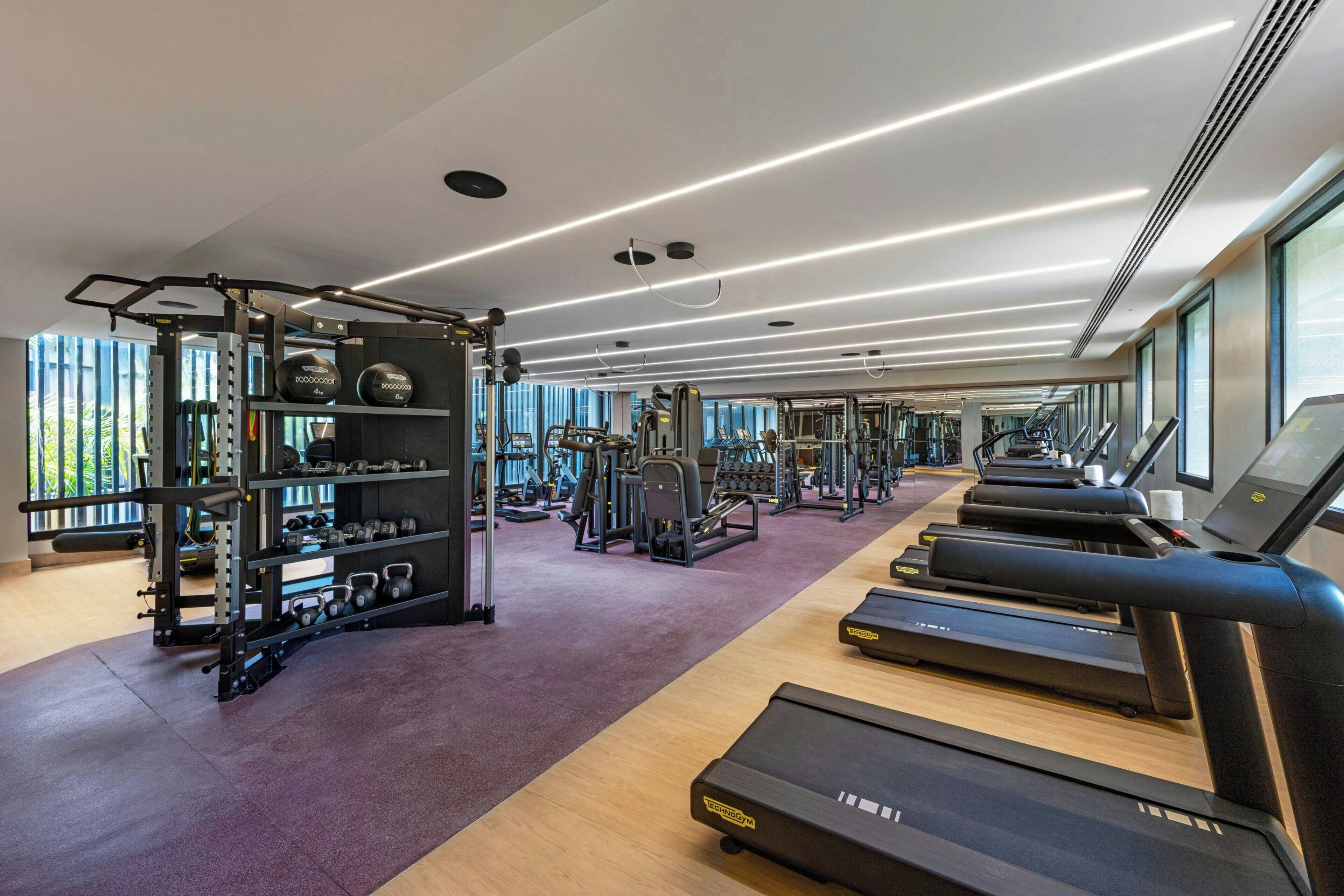 Un gimnasio moderno con cintas de correr, máquinas de pesas y pesas libres.