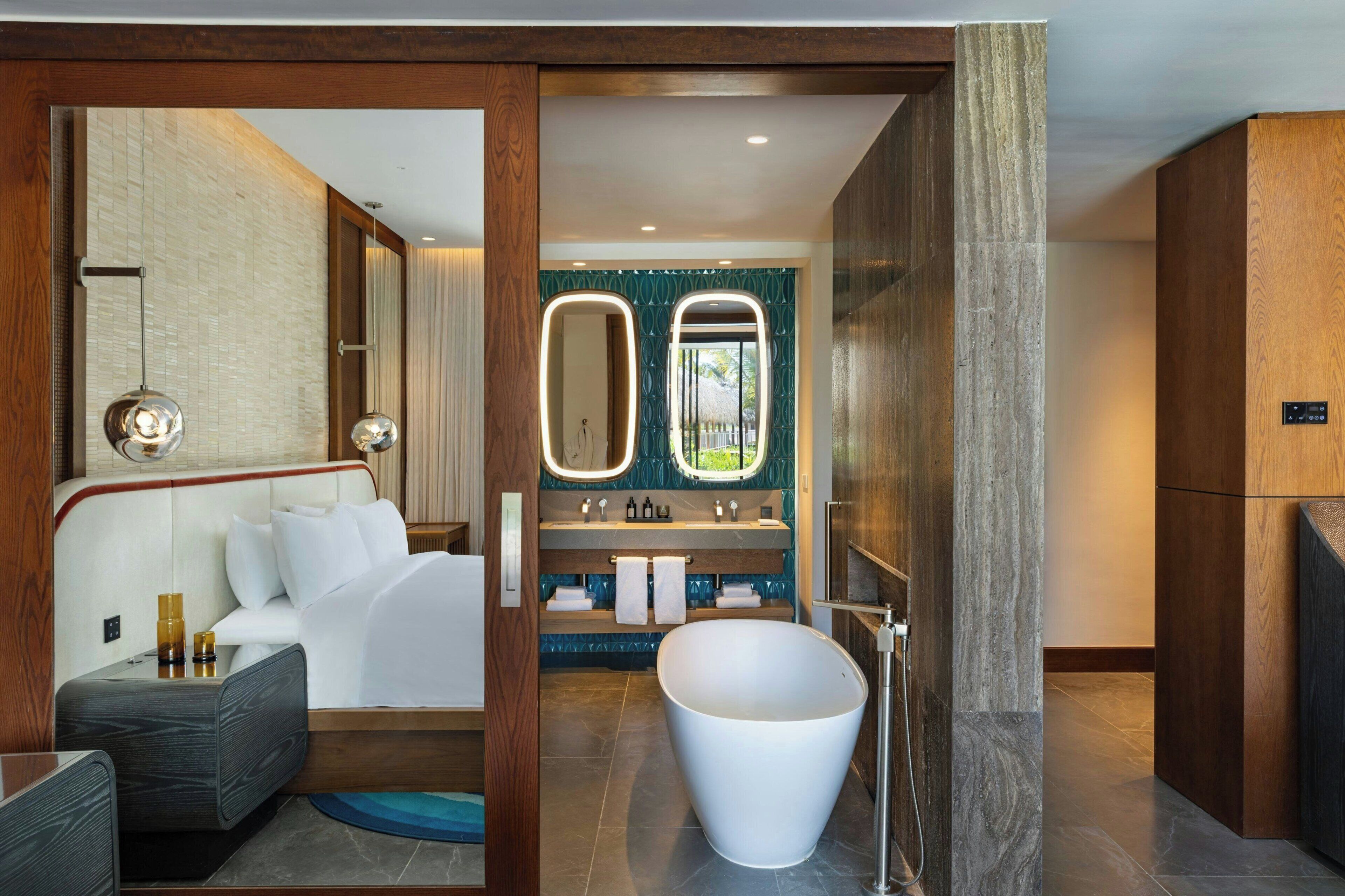 A modern bathroom with a freestanding bathtub, a vanity with two mirrors, and a seating area with a sofa and coffee table.