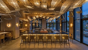 A modern bar area with a central bar, multiple seating options, and a ceiling with intricate light fixtures.