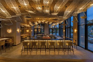 Zona de bar moderna con barra central, diversas opciones de asientos y un techo con elaboradas luminarias.