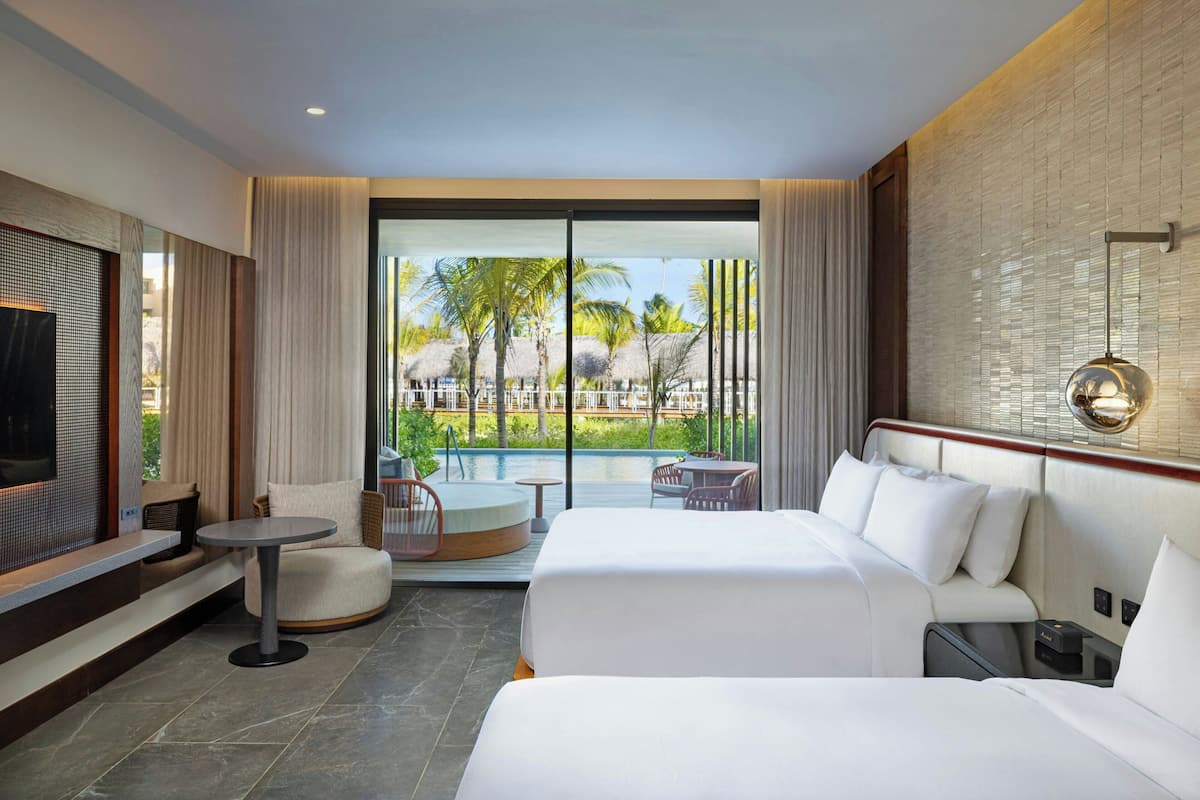 A hotel room with a large bed, a small round table, a TV, and a view of a pool and palm trees.