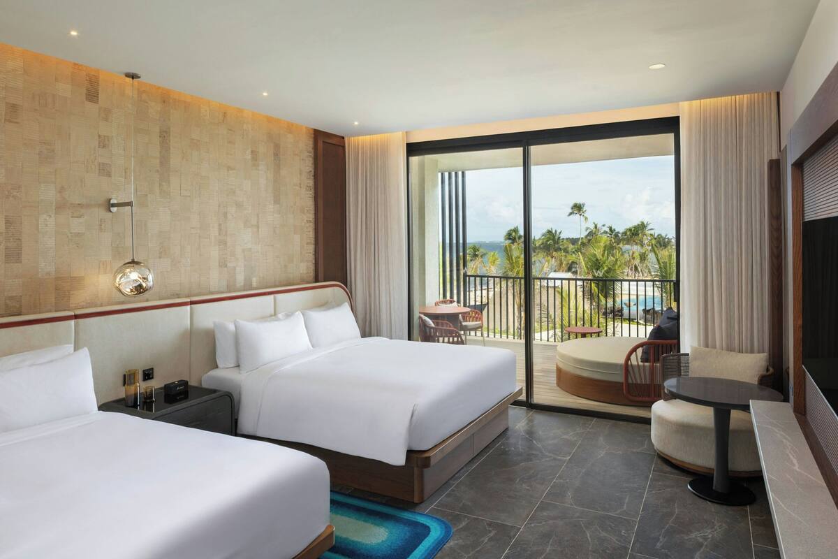 A hotel room with two beds, a balcony with a view of palm trees, and a TV.
