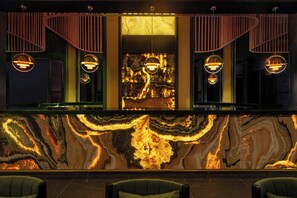 A bar area with a marble countertop, hanging pendant lights, and green upholstered chairs.