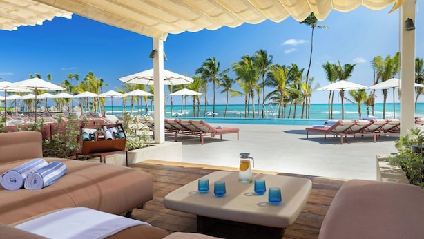 A beachside lounge with lounge chairs, umbrellas, and a pool view.