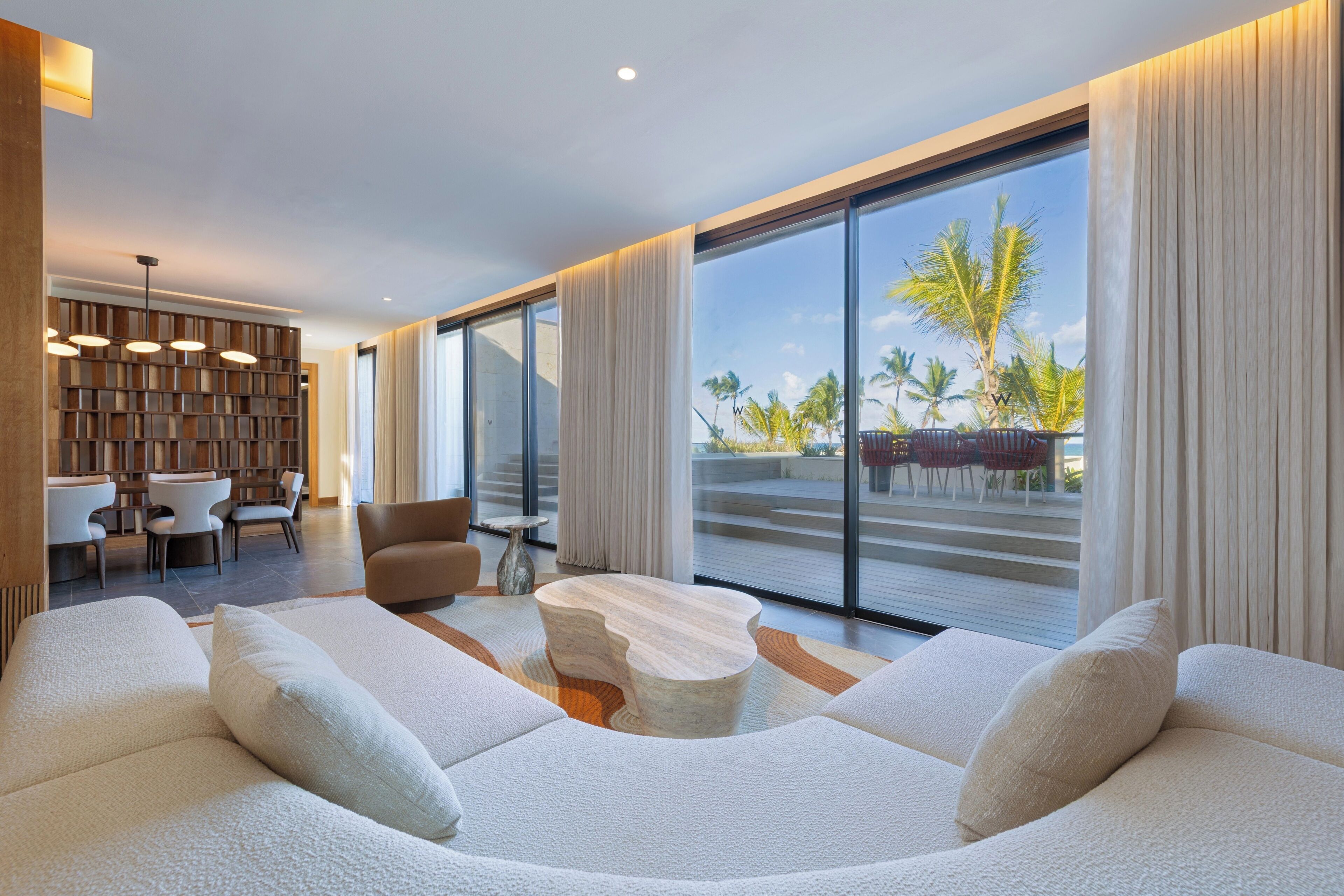 A modern living room with a large window, a seating area with sofas, a coffee table, and a dining area with chairs and a table.