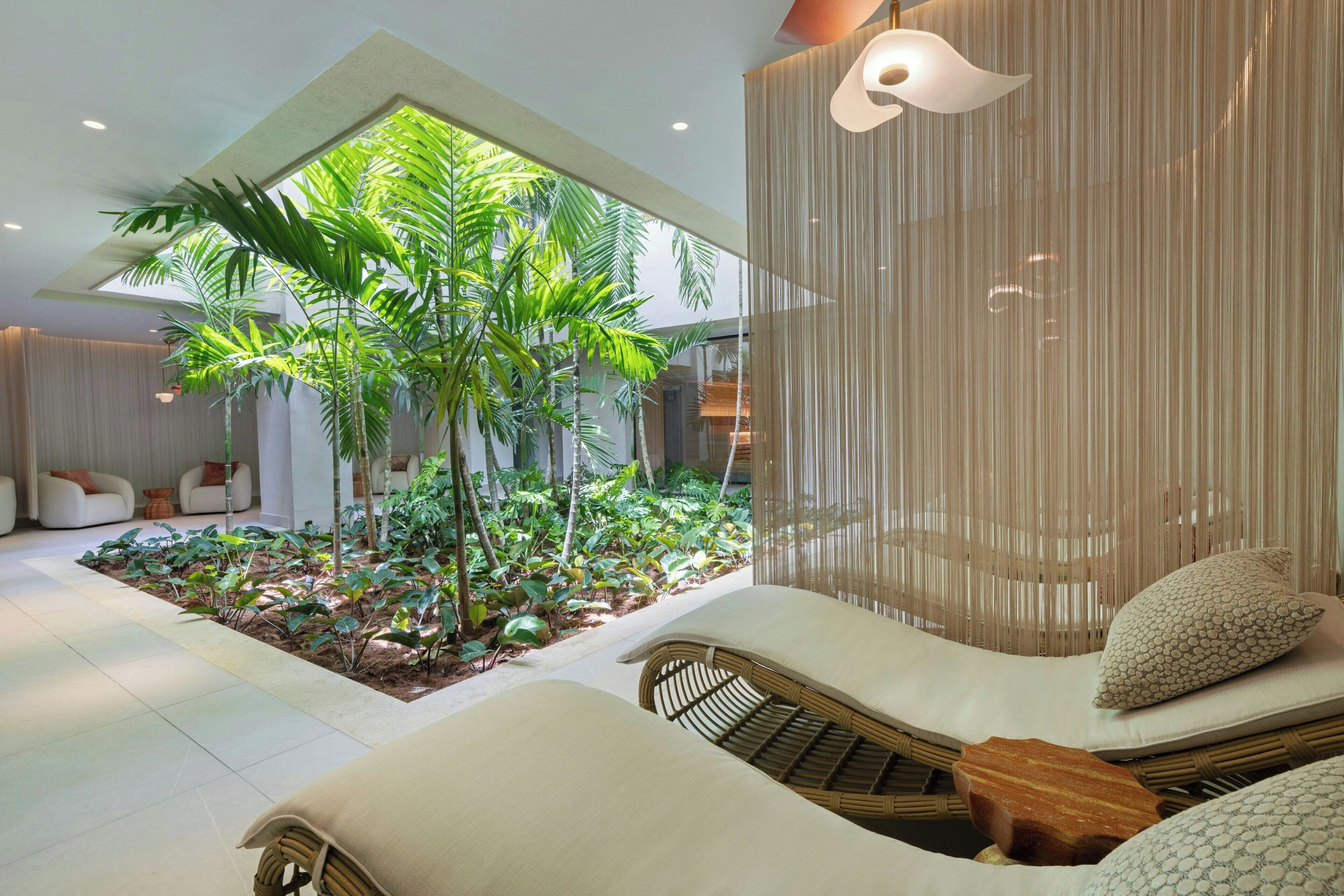 Een modern interieur met een centrale tuin, een zithoek met kussens, en een groot raam dat voor natuurlijk licht zorgt.