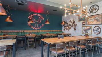 L’intérieur d’un restaurant, avec de nombreuses tables et chaises, un néon accroché au mur et diverses décorations murales.