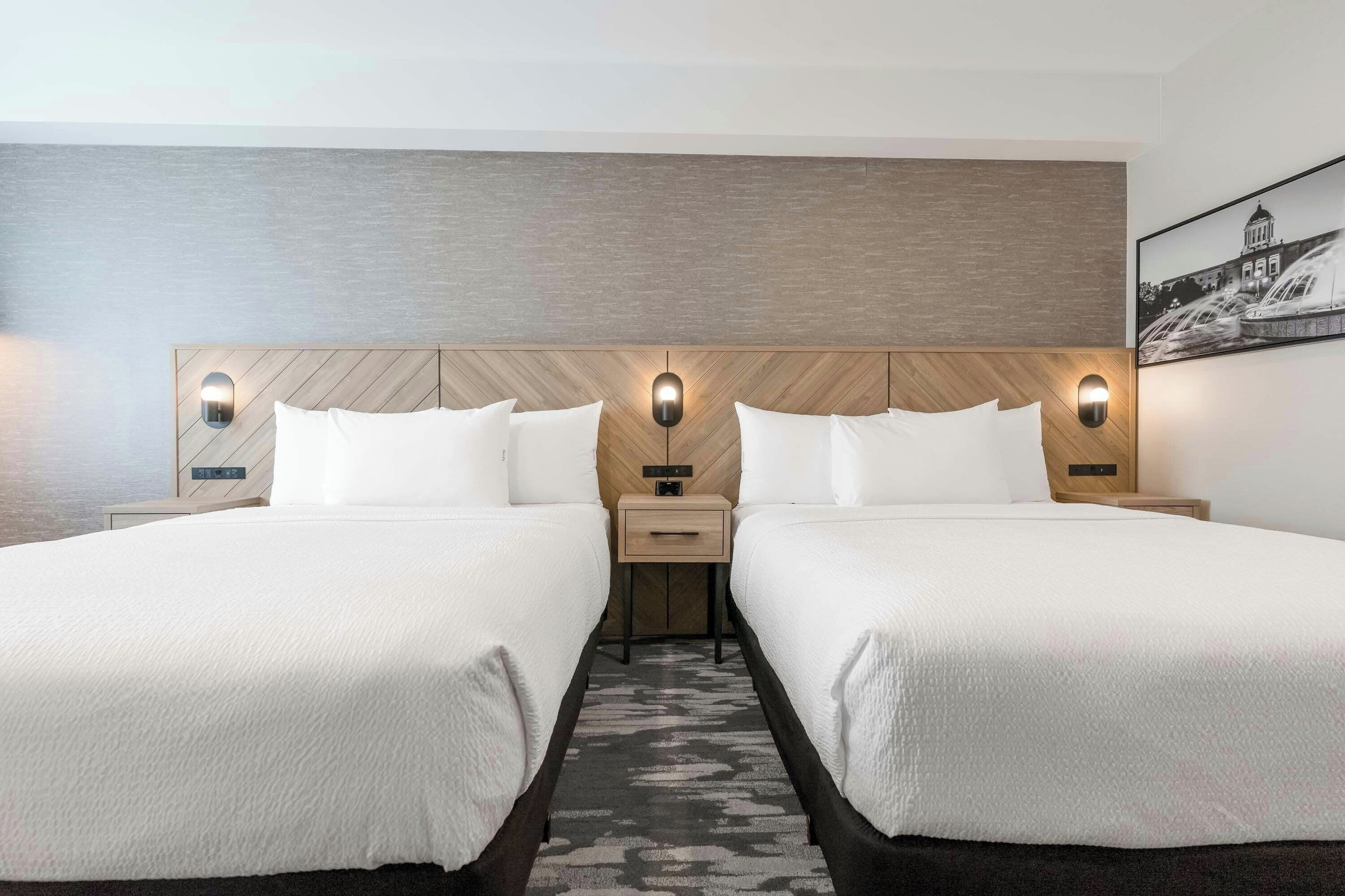 Een hotelkamer met twee bedden, een houten hoofdeinde, een nachtkastje en een aan de muur hangend schilderij.