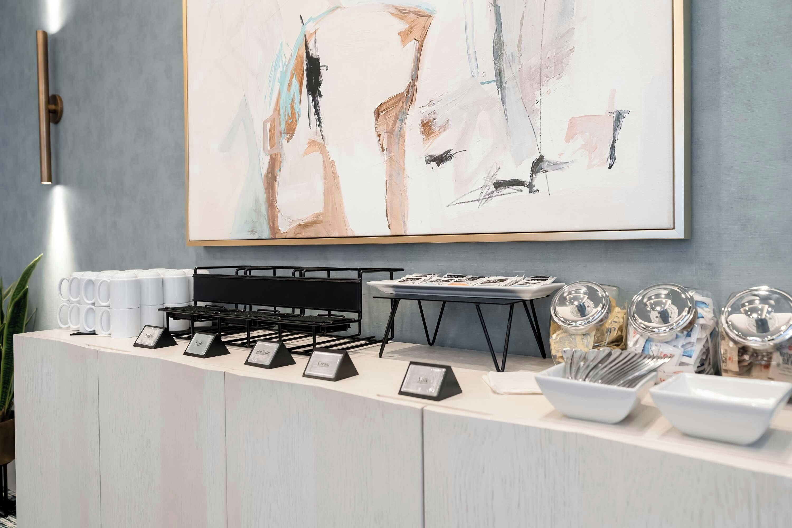 A counter with coffee and cream dispensers, a hot water station, and a tray with items.