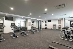 Un gimnasio con cintas de correr, máquinas de pesas y pesas sueltas.