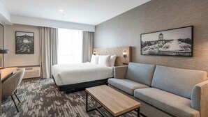 Une chambre d’hôtel avec un lit, un canapé, une table basse et un bureau. Il y a deux tableaux accrochés au mur.