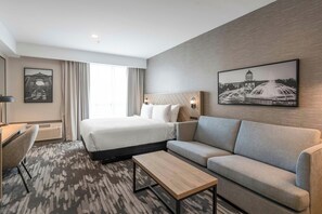 Habitación de hotel con cama, sofá, mesa de centro y escritorio. Hay dos cuadros en la pared.
