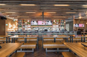 Interior de un restaurante con techos de paneles de madera, una zona de bar y diferentes disposiciones de asientos.
