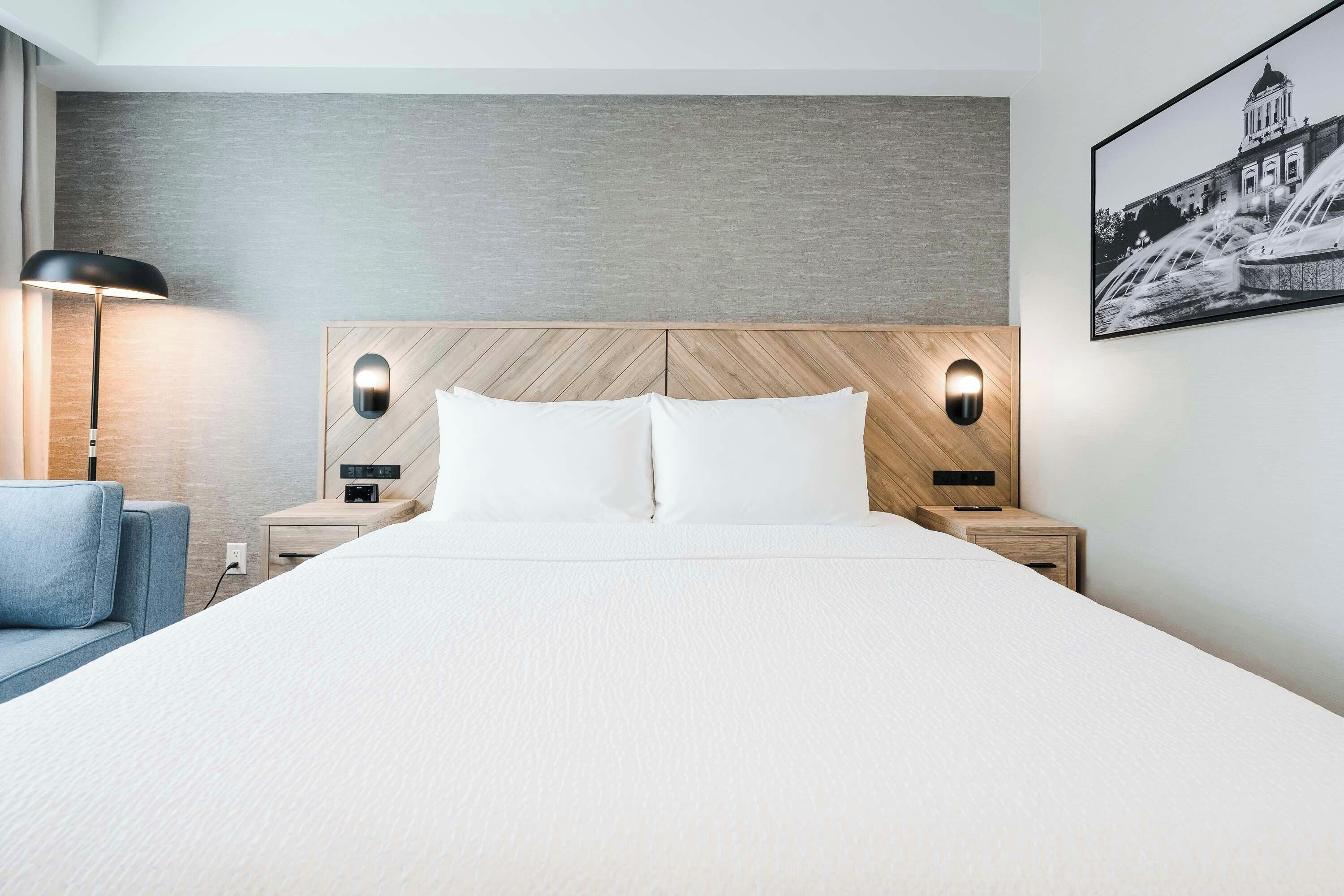 A hotel room with a large bed, two bedside tables, a lamp, and a wall-mounted picture.