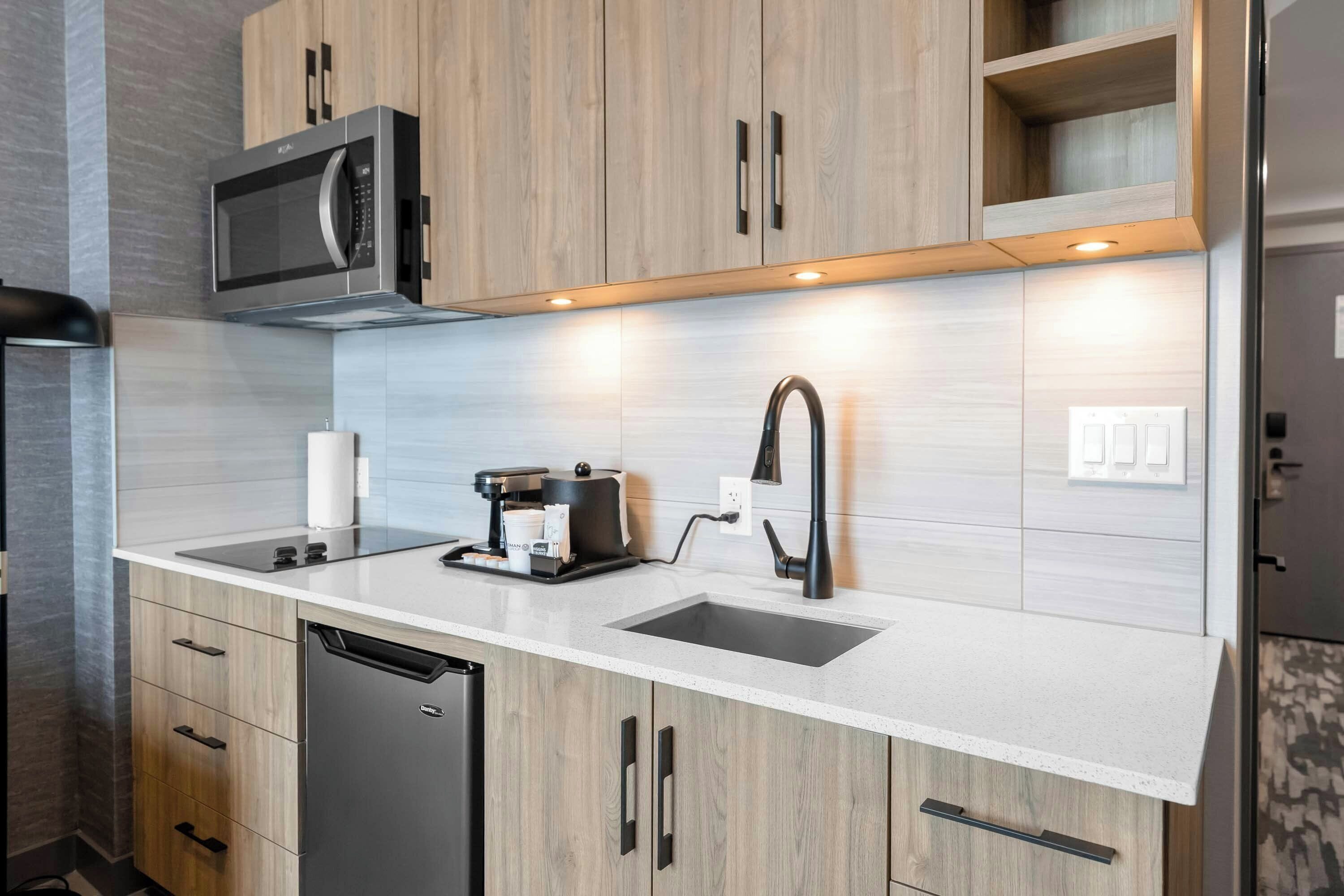 A modern kitchen with wooden cabinets, a built-in microwave, a coffee machine, and a sink.