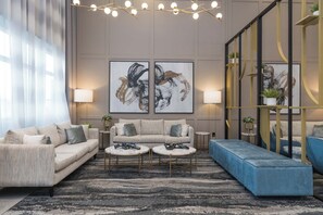 A modern living room with a beige sofa, two round coffee tables, and a blue ottoman. There are two framed abstract paintings on the wall, a chandelier, and a plant on a shelf. - Sandman Signature Winnipeg Airport Hotel & Suites (Winnipeg)
