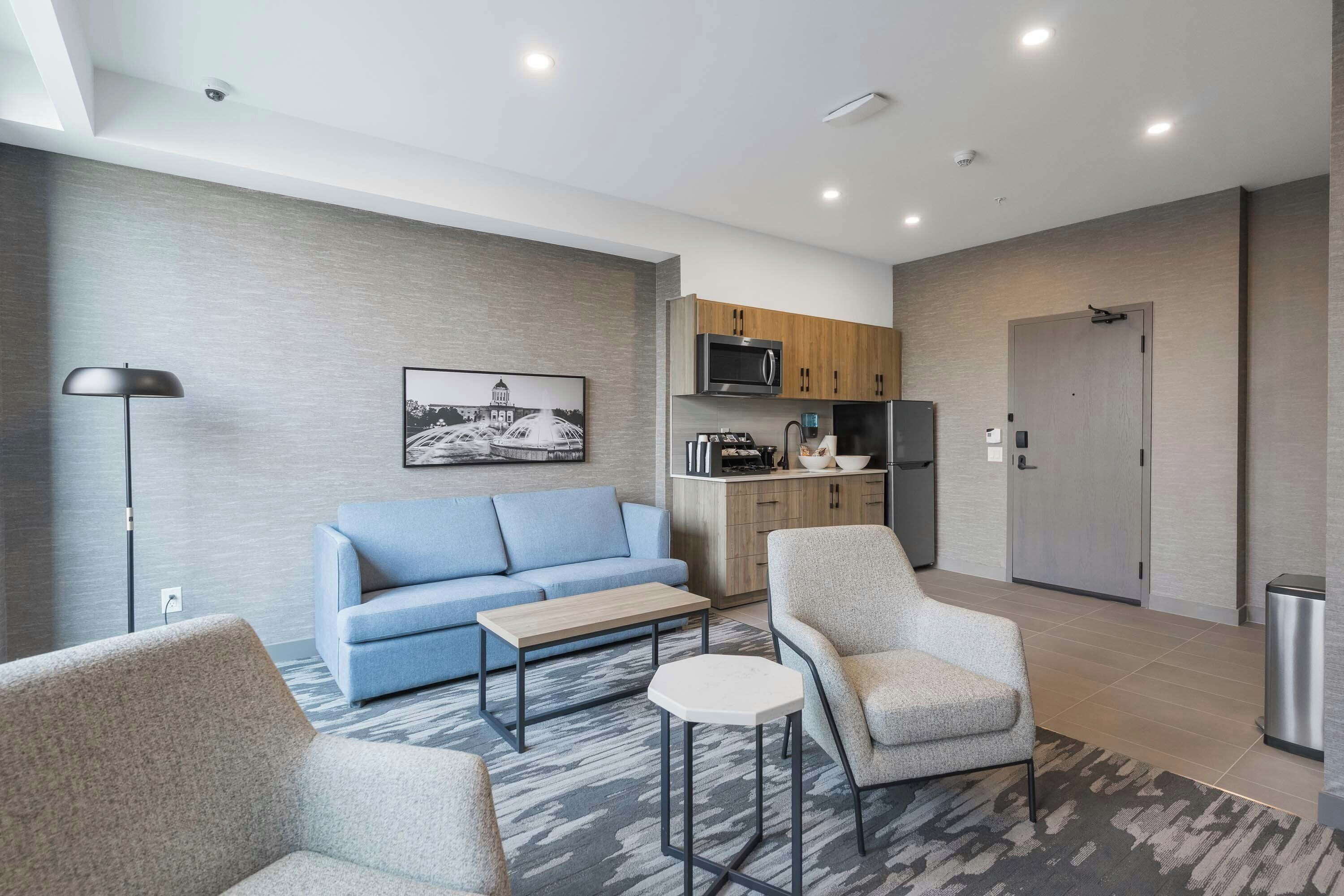 A modern living room with a sofa, armchairs, a coffee table, and a kitchen area with appliances.