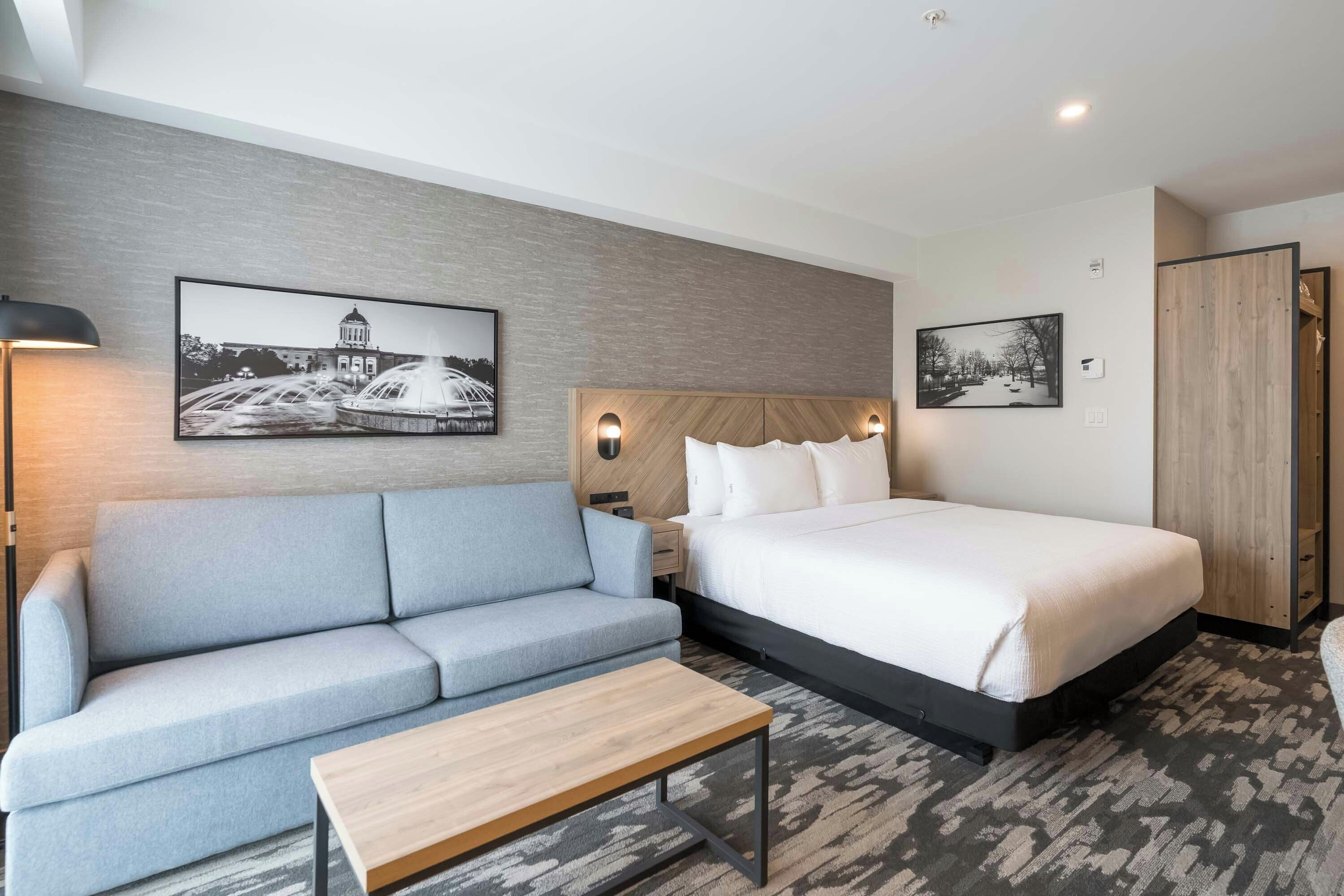 A hotel room with a bed, a sofa, a small table, and two wall-mounted lamps.