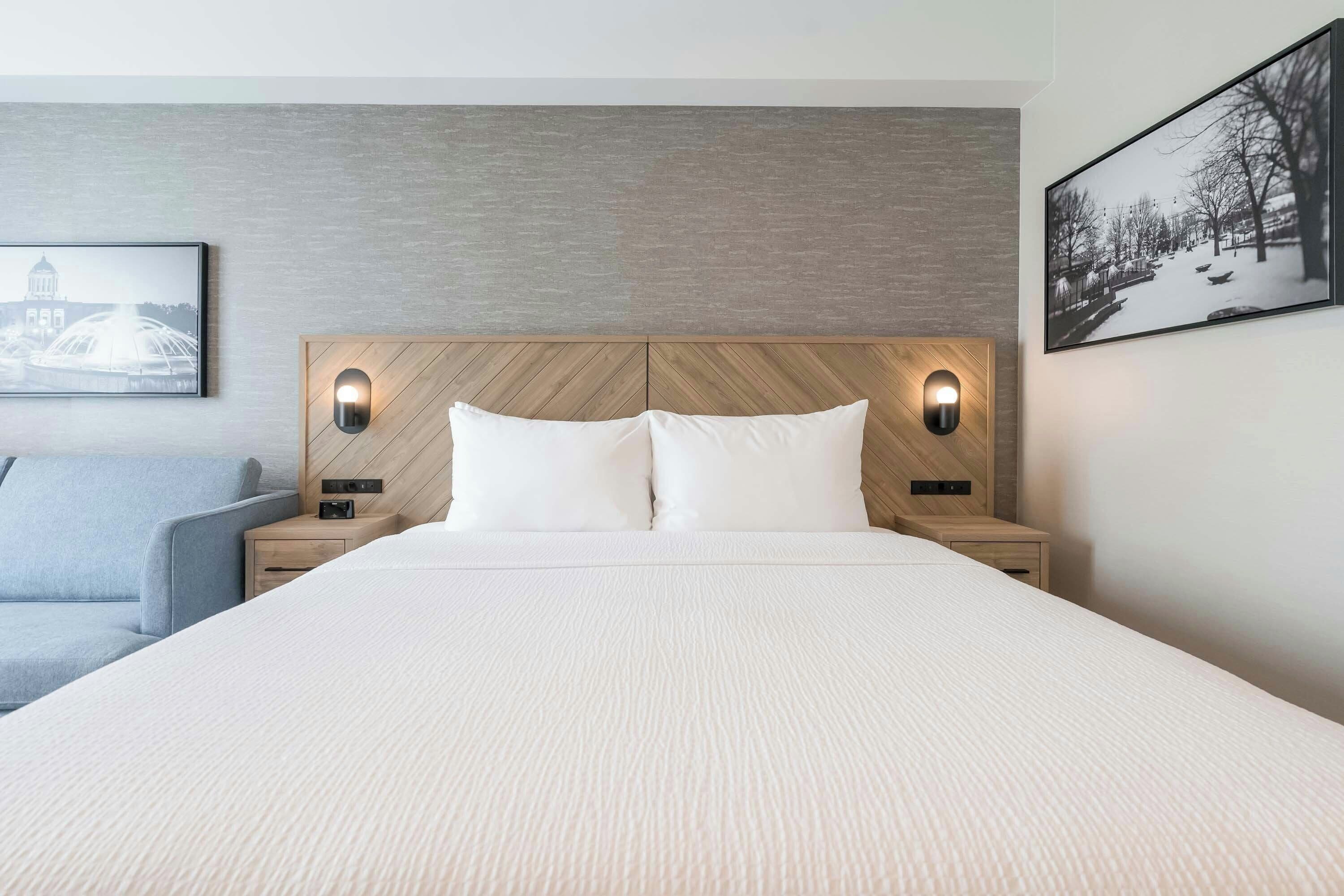 A hotel room with a large bed, two bedside tables, a headboard with built-in lighting, and two framed pictures on the walls.