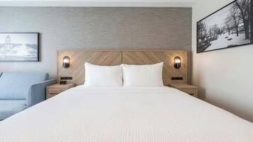A hotel room with a large bed, two bedside tables, a headboard with built-in lighting, and two framed pictures on the walls.