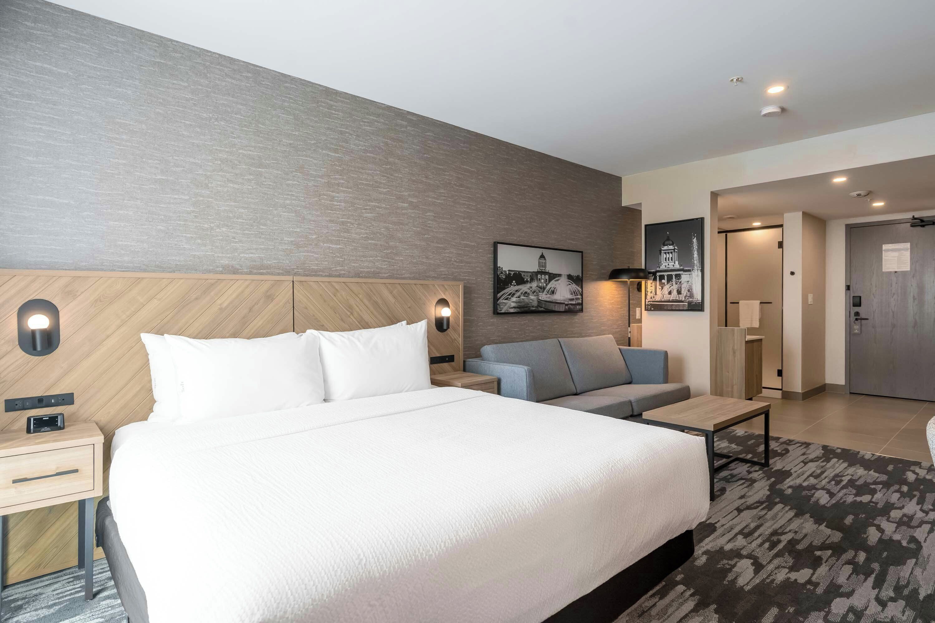 Une chambre d’hôtel moderne équipée d’un grand lit, d’un canapé, d’un bureau et d’un téléviseur fixé au mur.